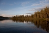 Die von den letzten Sonnestrahlen des Tages beschienenen Bäume spiegeln sich im glatten See